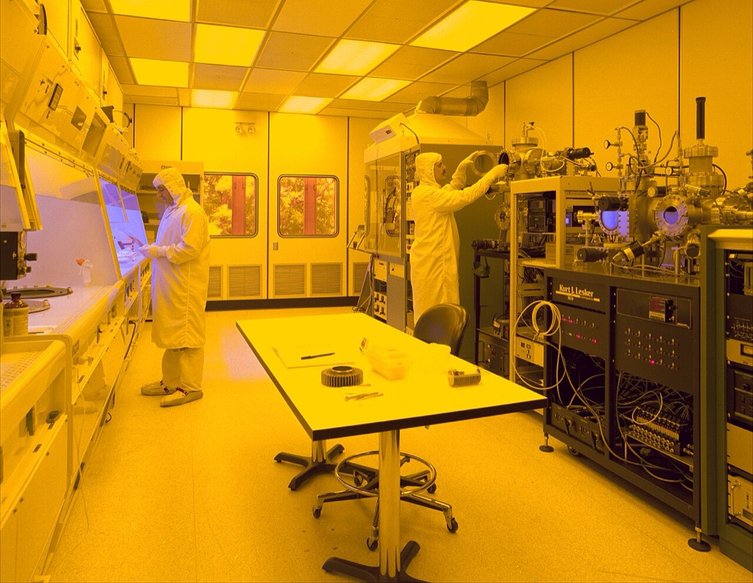 Technicians working in a semiconductor clean room under yellow lithography lighting
